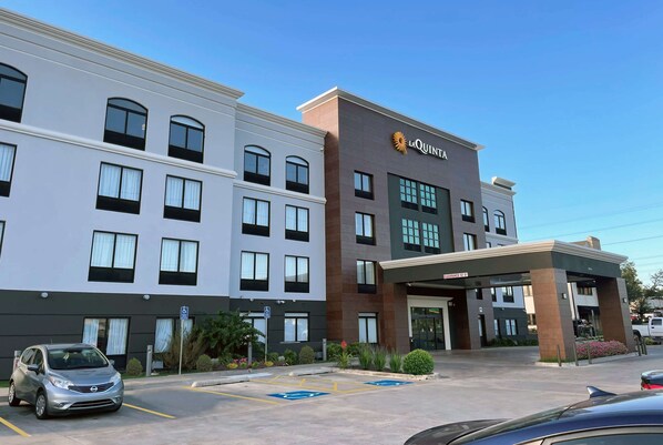 Un hotel con una fachada moderna, un llamativo letrero de 'La Quinta' y un estacionamiento con espacios reservados para discapacitados.