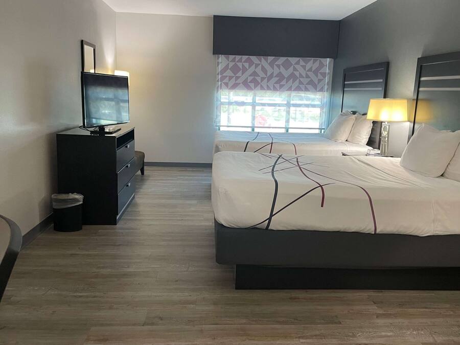 A hotel room with a large bed, a TV on a dresser, and a window with patterned curtains.