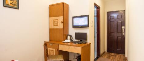 Una camera d'albergo compatta con una scrivania in legno, un computer, una sedia, un letto con copripiumino rosso e una porta.