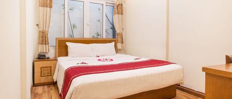A neatly arranged bedroom with a wooden bed, a bedside table, a small desk, and a window with curtains.