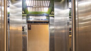 An elevator interior with metallic walls, a patterned floor, and a green ceiling with light fixtures. - Hanoi Charming House (Hanoi)