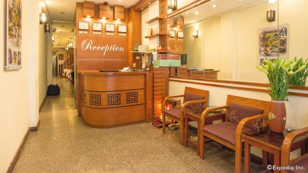 A reception area with a wooden reception desk, seating area with chairs, and a wall with clocks and a poster. - Hanoi Charming House (Hanoi)