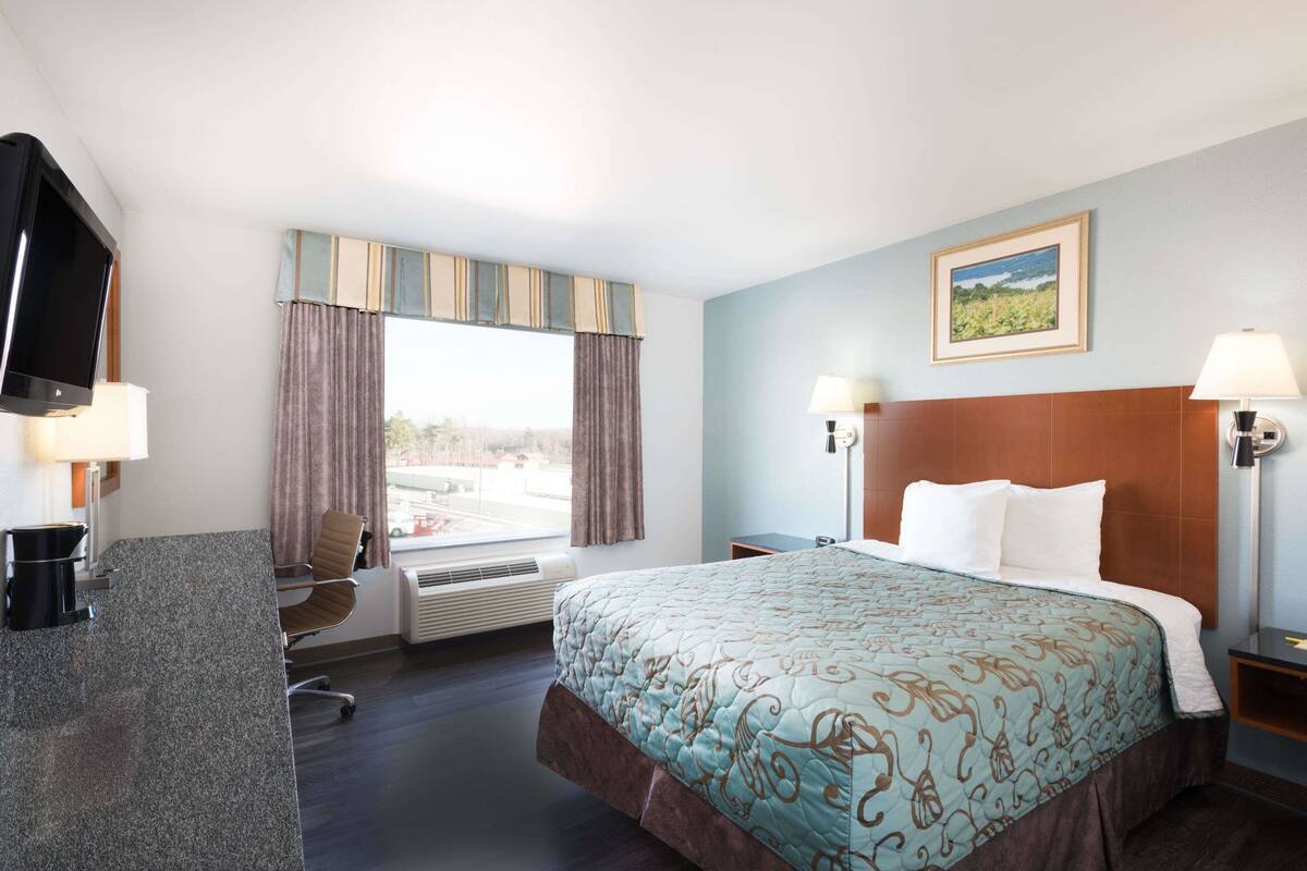 Habitación de hotel con cama, escritorio con computadora, televisor y ventana con cortinas.