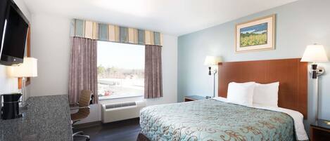 A hotel room with a bed, a desk with a computer, a TV, and a window with curtains.
