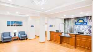 Een receptie met een Days Inn bord, twee blauwe fauteuils, een houten balie en een kroonluchter.