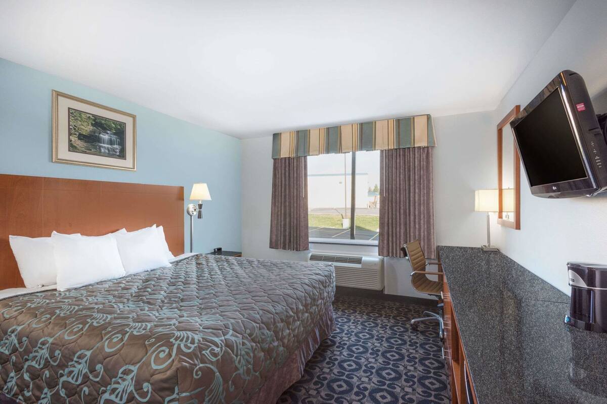 Una habitación de hotel con una cama grande, un escritorio, un televisor y una ventana con cortinas.