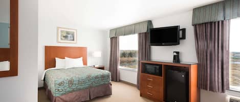 Une chambre d’hôtel équipée d’un lit, d’une télévision, d’un bureau avec un réfrigérateur et d’une fenêtre avec des rideaux.