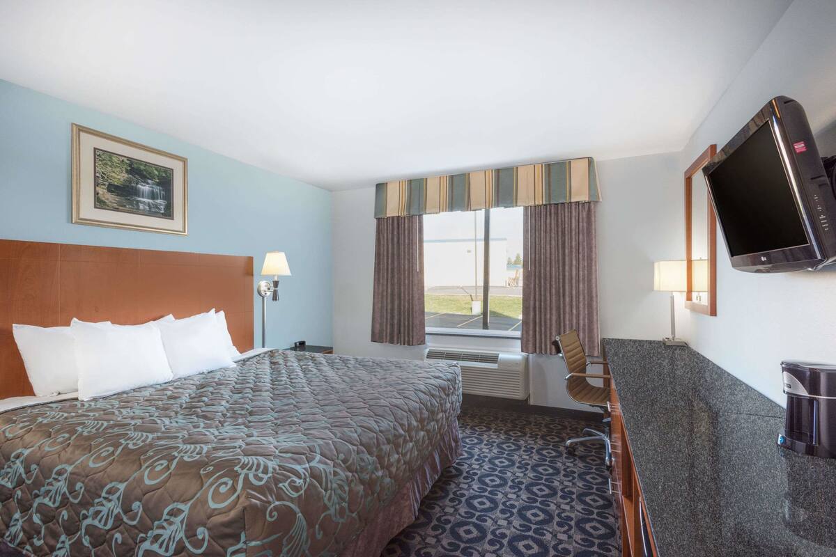 Una habitación de hotel con una cama grande, un escritorio, un televisor y una ventana con cortinas.