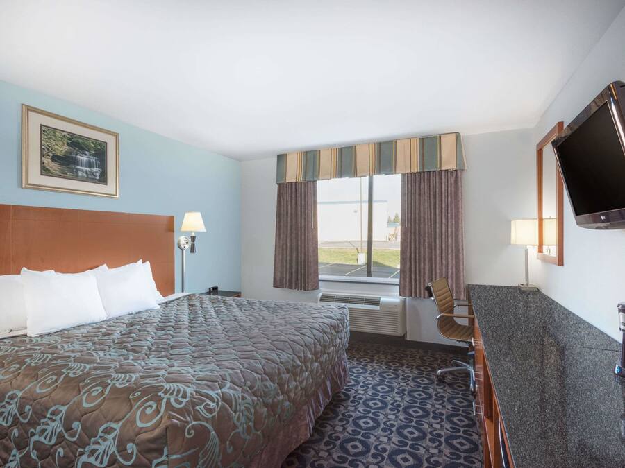 A hotel room with a large bed, a desk, a TV, and a window with curtains.