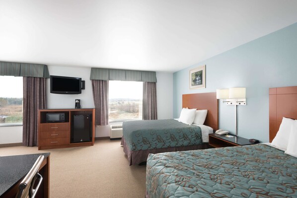 Habitación de hotel con dos camas, un escritorio con computadora, televisor y ventana con cortinas.