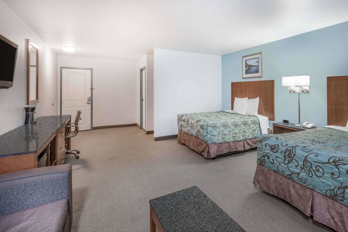 Una habitación de hotel con dos camas, un escritorio, una silla, un televisor y la puerta del baño.