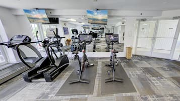 A gym with treadmills, stationary bikes, and a TV screen.