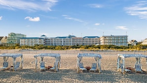 Un hotel frente a la playa con varios balcones, sombrillas y sillones de descanso.