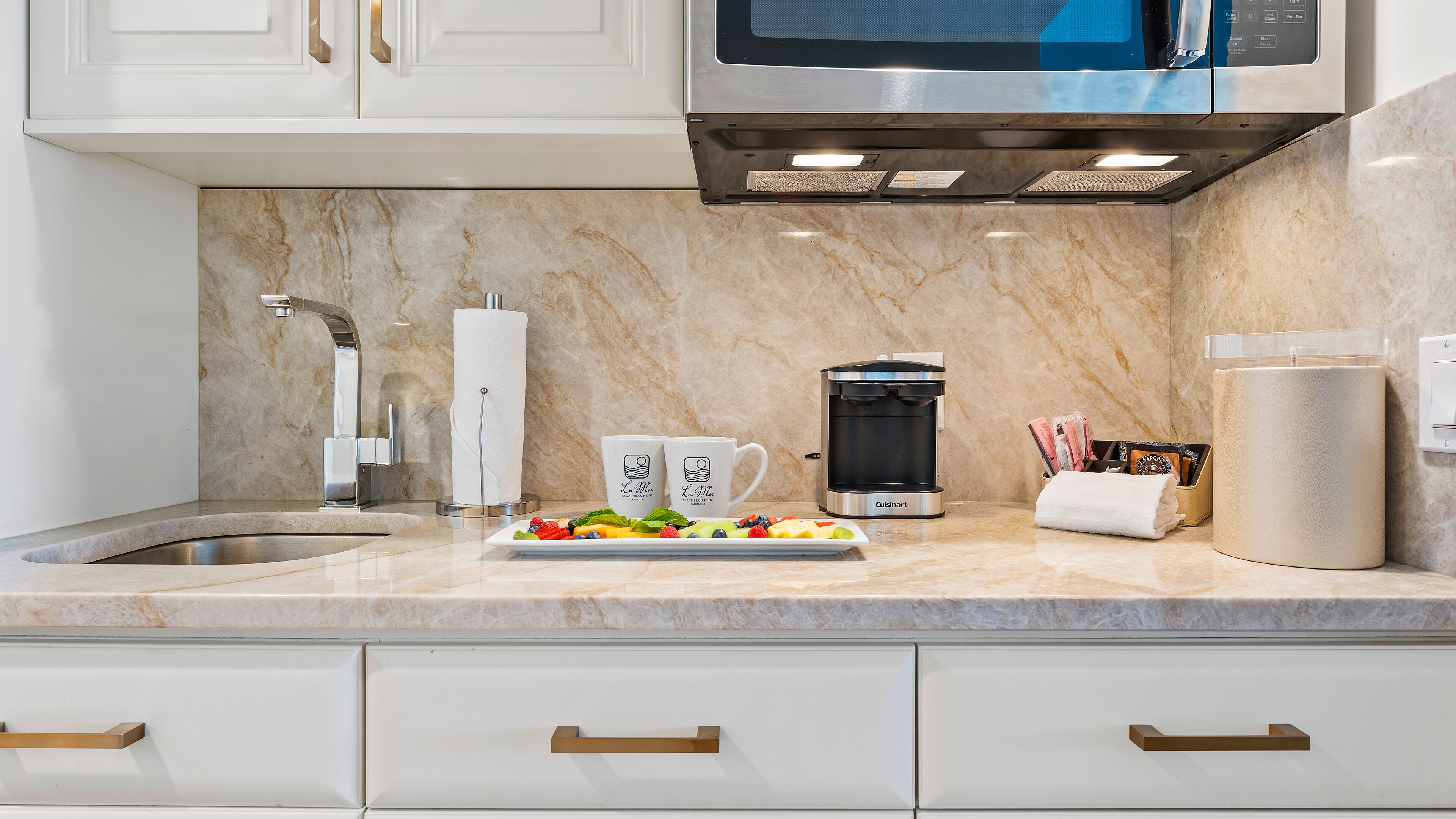 A modern kitchen with a marble countertop, stainless steel appliances, and white cabinetry.
