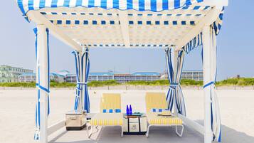 Una cabaña de playa con dos sillones reclinables y una mesa, una maleta y una botella en la terraza.