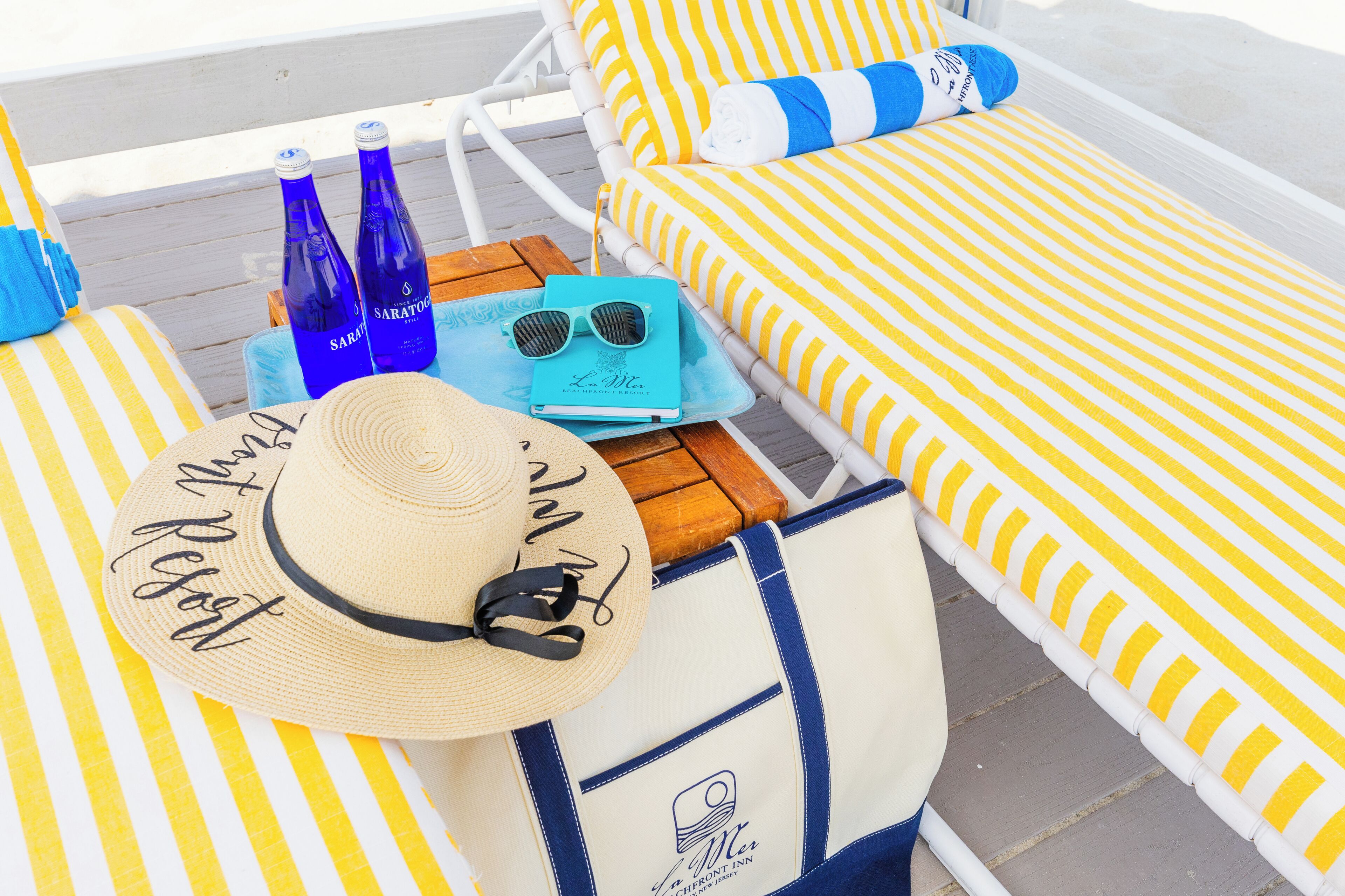 A sun lounger with striped cushions, a hat, sunglasses, and two bottles of Saratoo water.