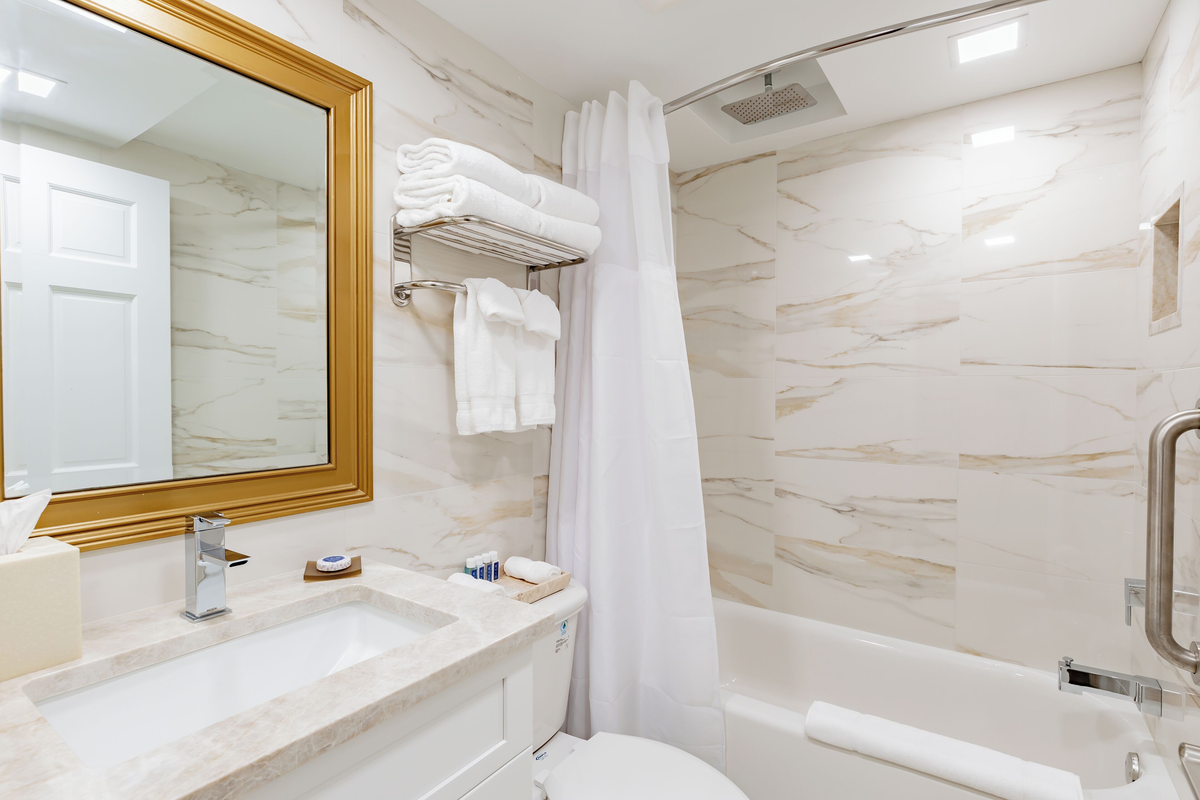 A modern bathroom with a marble sink, a large mirror, a shower with a glass door, and a toilet.