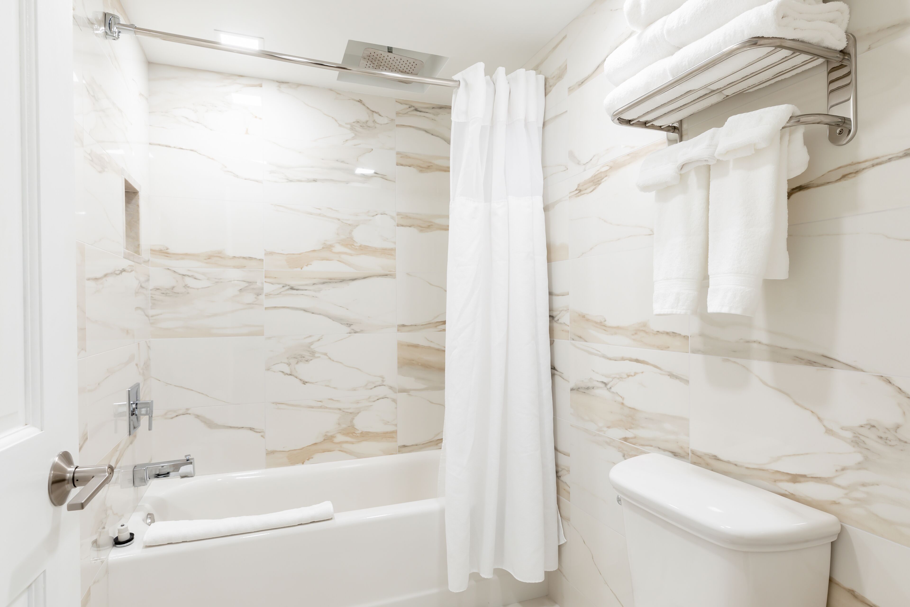A bathroom with a marble wall, a bathtub, a toilet, and a shower curtain.