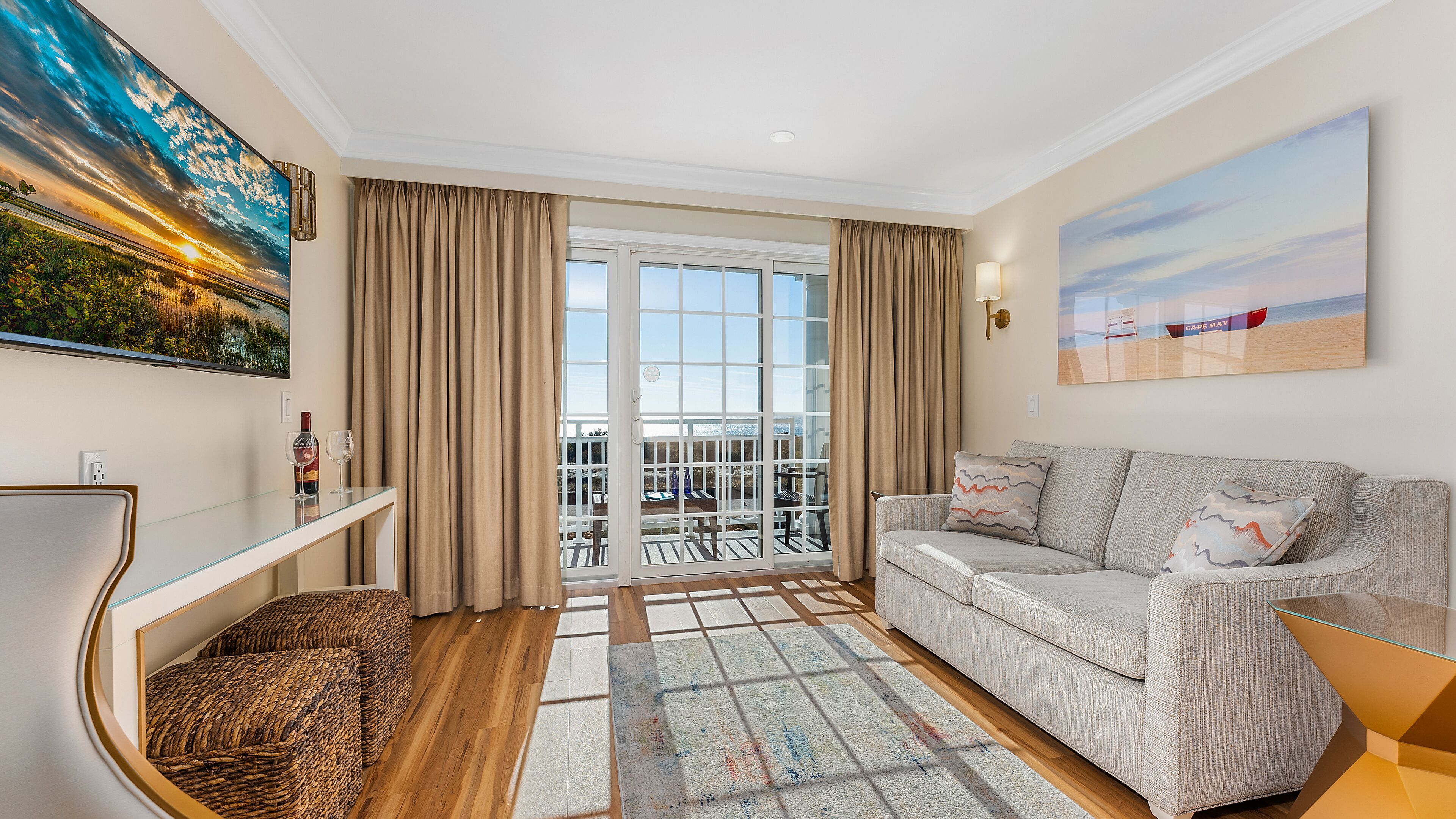 Een moderne woonkamer met een glazen deur die leidt naar een balkon, een bank, een salontafel en een schilderij van een zonsondergang.