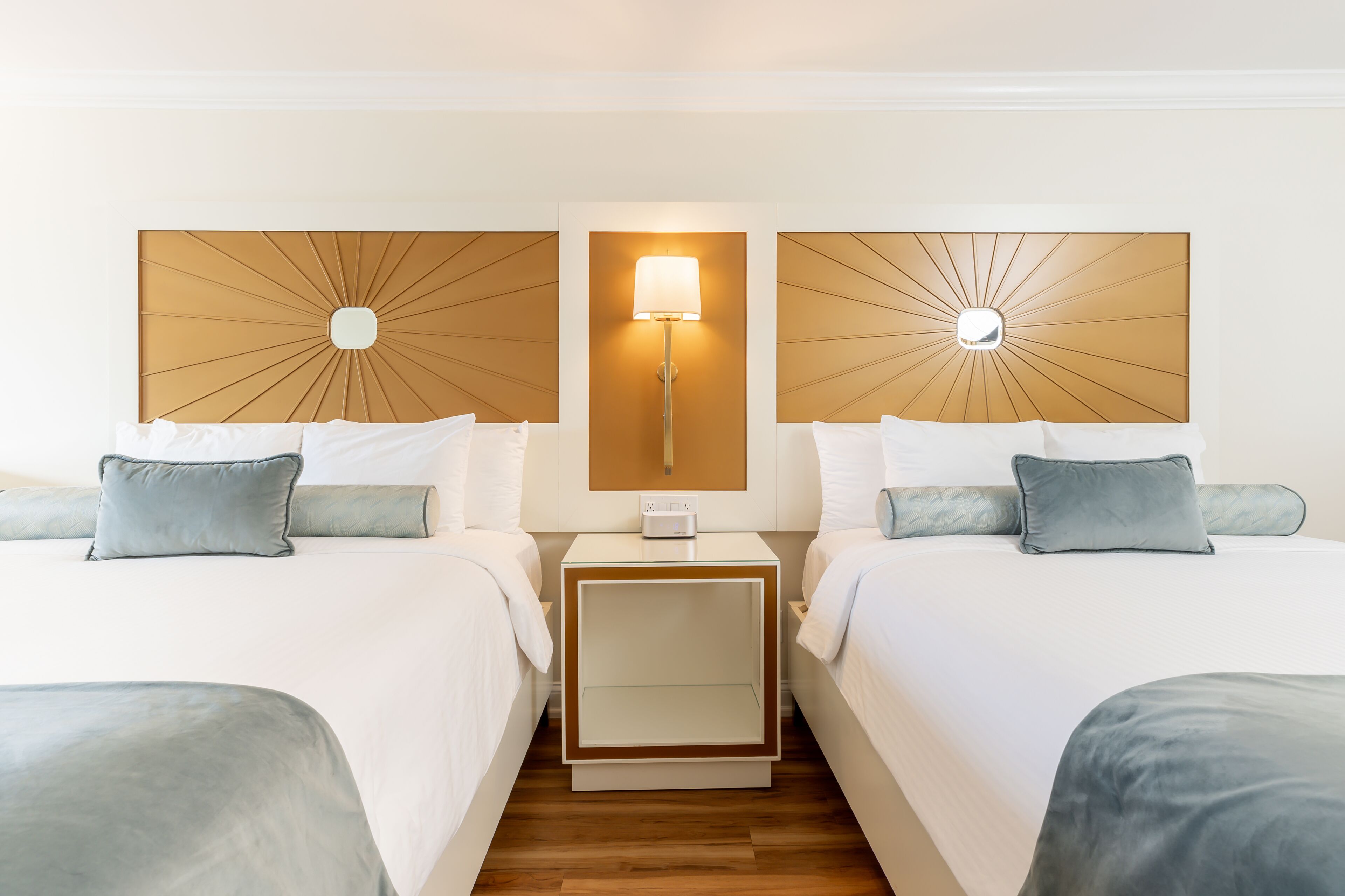 A hotel room with two beds, a nightstand with a lamp, and a modern headboard design.