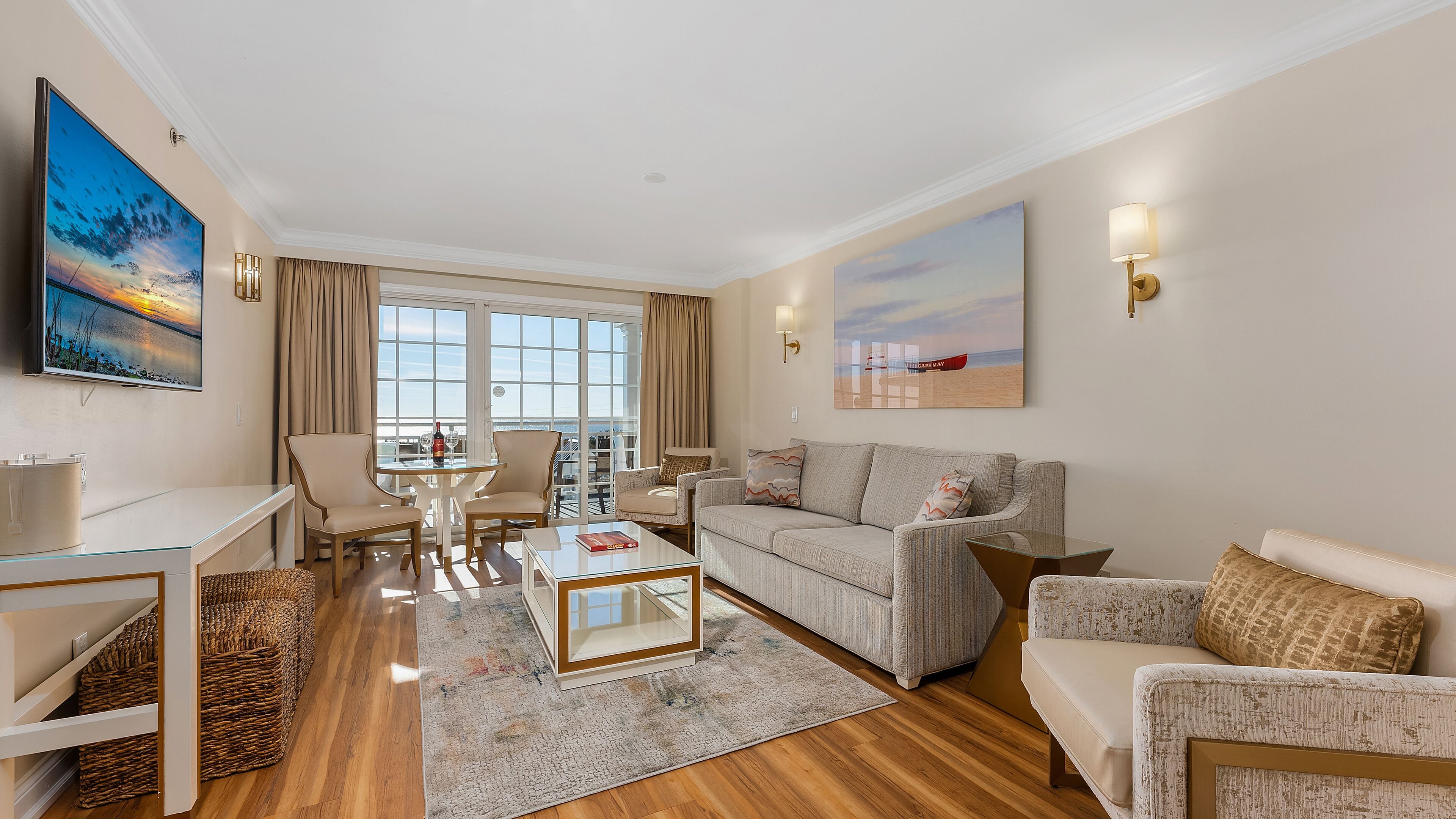 Una sala de estar moderna con un sofá, sillones, una mesa de centro y un televisor. Se ve una ventana grande con vistas al mar.
