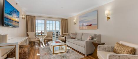 Una sala de estar moderna con un sofá, sillones, una mesa de centro y un televisor. Se ve una ventana grande con vistas al mar.
