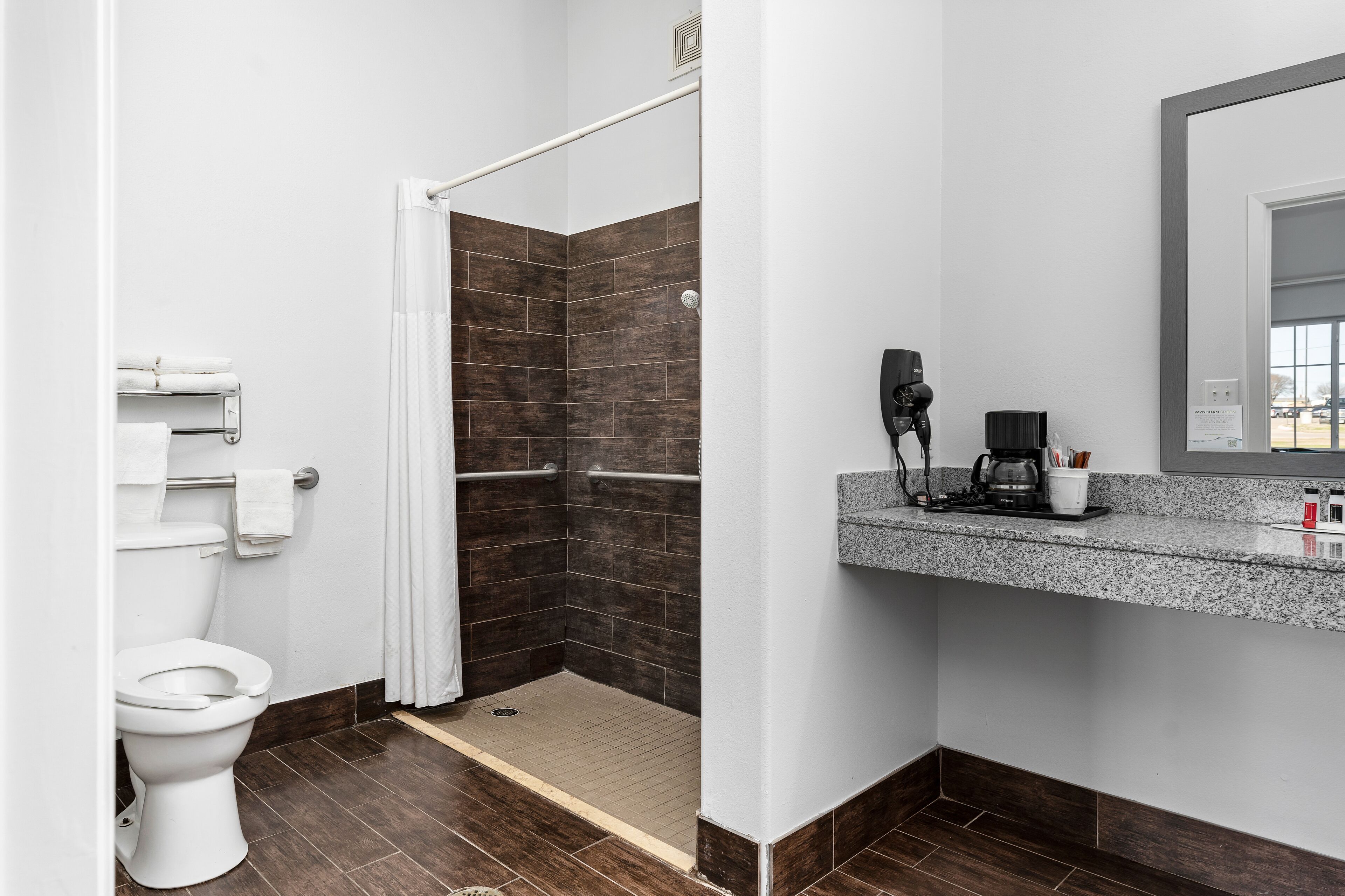 Un baño moderno con inodoro blanco, ducha con puerta blanca y encimera de granito con cafetera.