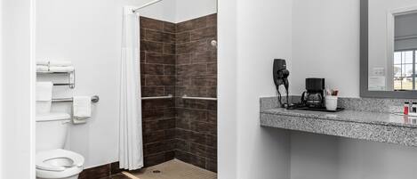 A modern bathroom with a white toilet, a shower with a white door, and a granite countertop with a coffee maker.