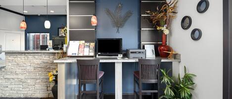 A modern kitchen with a stone accent wall, two bar stools, a desktop computer, and a potted plant.