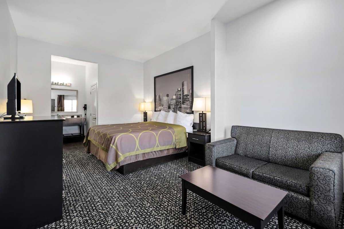 A hotel room with a bed, a sofa, a desk, and a cityscape painting on the wall.