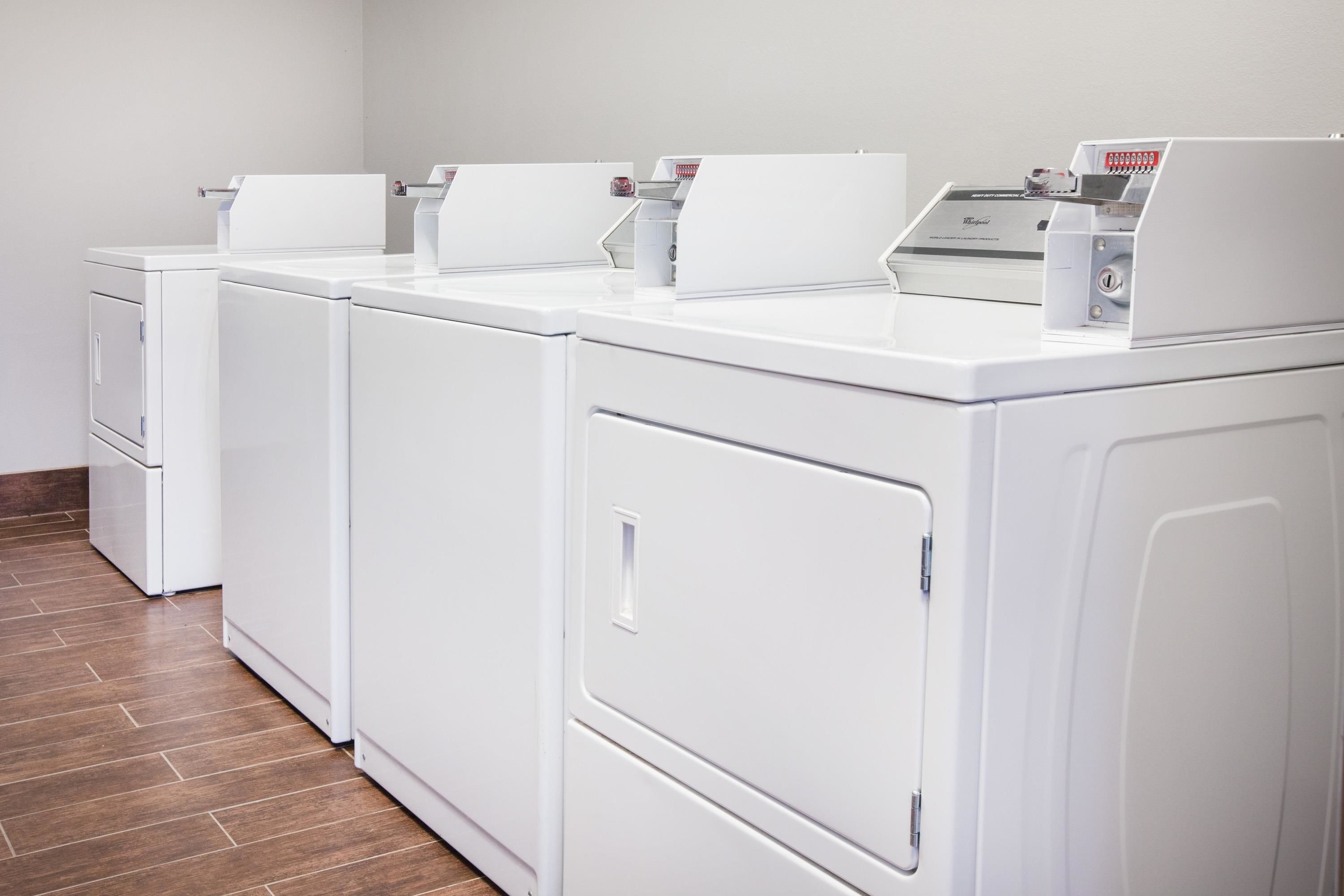A row of white front-loading washers and dryers in a laundry room.