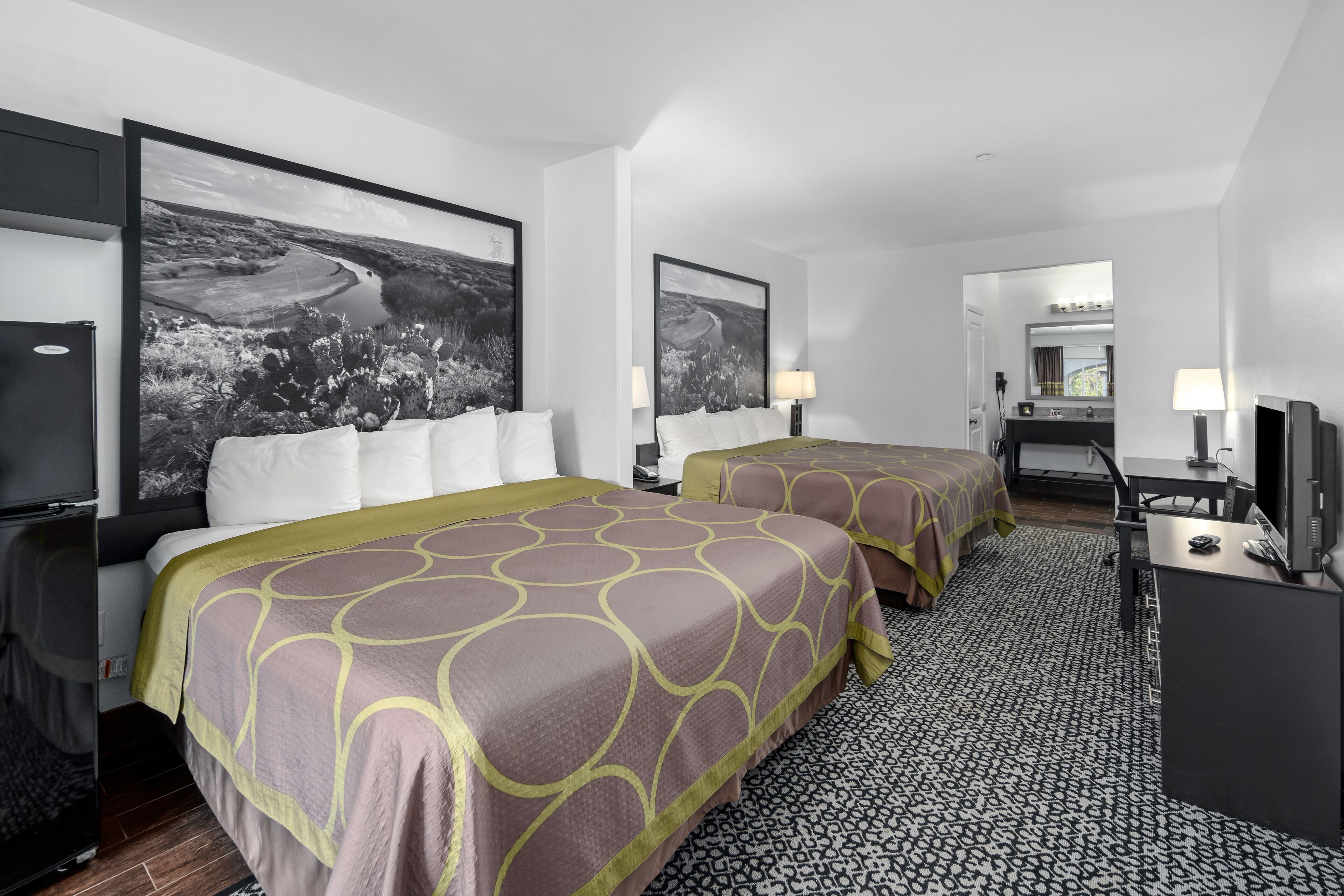 A hotel room with two beds, a desk, a TV, and artwork on the walls.