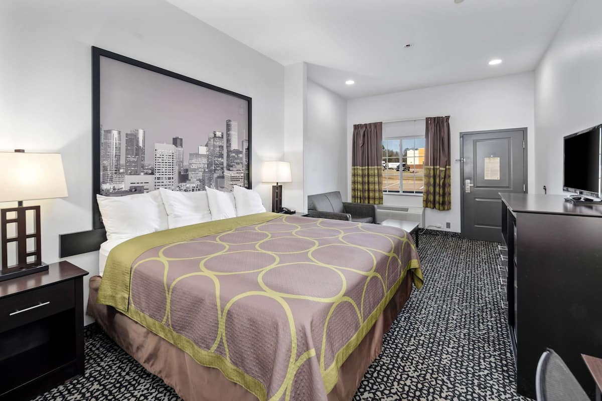 A hotel room with a large bed, two bedside tables with lamps, a desk with a chair, a television, and a cityscape view.