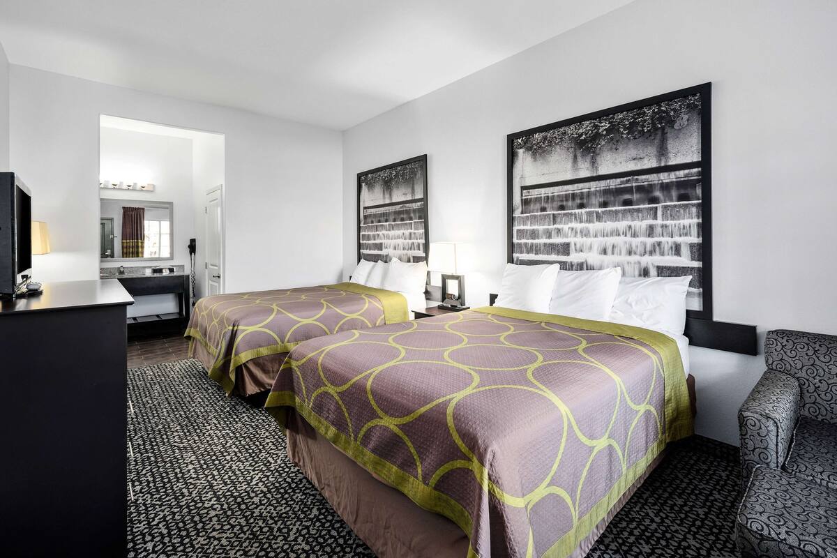 A hotel room with two beds, a desk, a chair, and a large window.