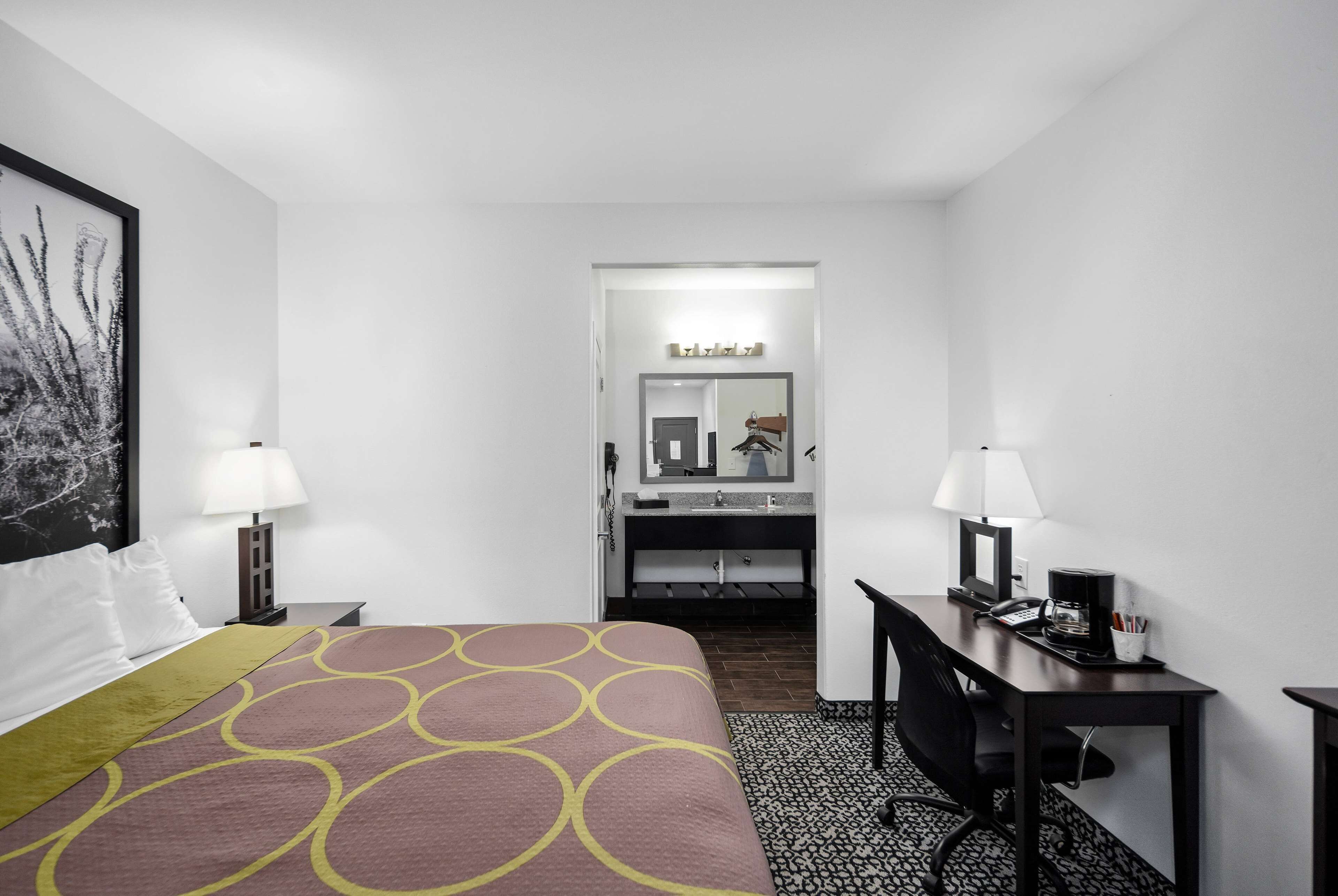 Een hotelkamer met een bed, een bureau, een stoel, een bureaulamp, een telefoon en een spiegel.