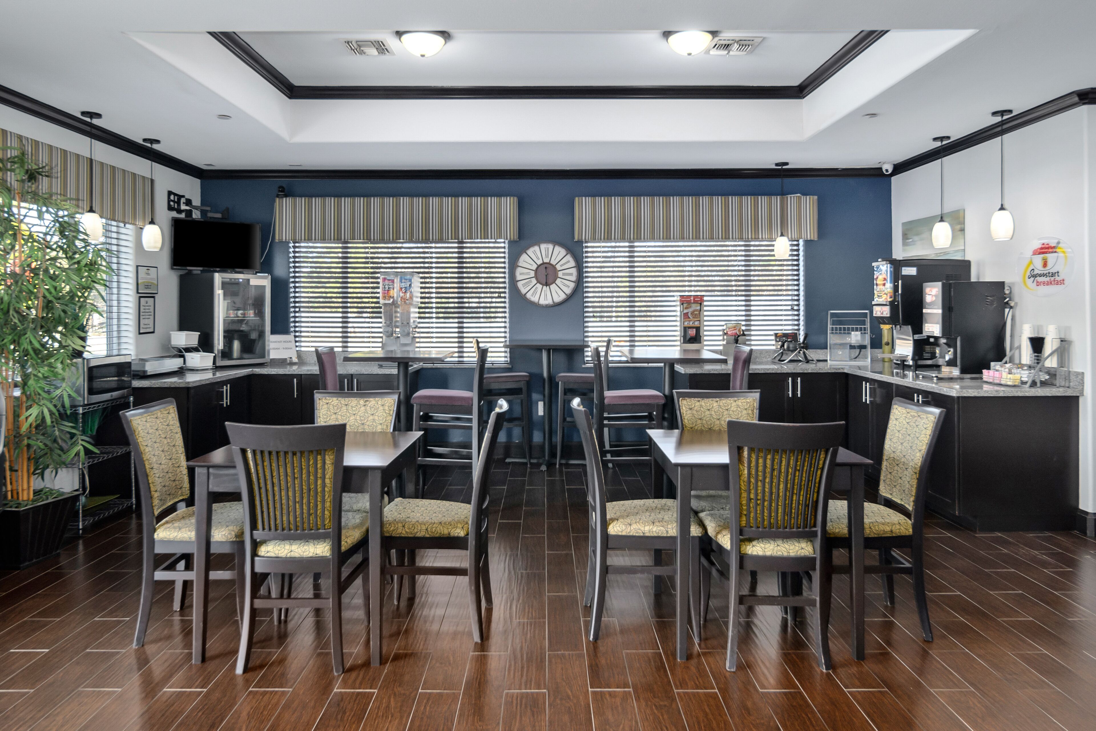 A modern kitchen with a dining area, featuring a central clock, striped window treatments, and a coffee machine.