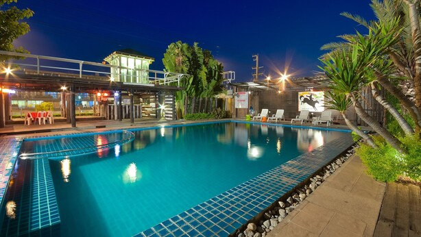 A swimming pool with a tiled edge, surrounded by a wooden deck and palm trees. - Season Palace Huahin Hotel (Cha-am)