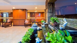 A well-lit indoor space with wooden furniture, a water feature, and a television mounted on the wall. - Season Palace Huahin Hotel (Cha-am)