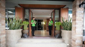 A hotel entrance with two staff members standing in the doorway, large potted plants on either side, and a wooden-framed entrance. - Season Palace Huahin Hotel (Cha-am)