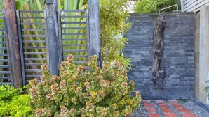 A garden with a wooden fence, a stone wall, and a small bush with pink flowers. - Season Palace Huahin Hotel (Cha-am)