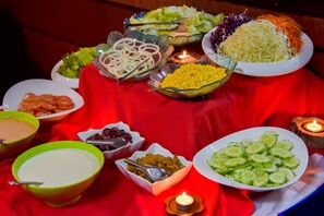 Una mesa con diversos platos y cuencos de comida, incluyendo ensaladas, verduras y un tazón de sopa, sobre un mantel rojo con velas.