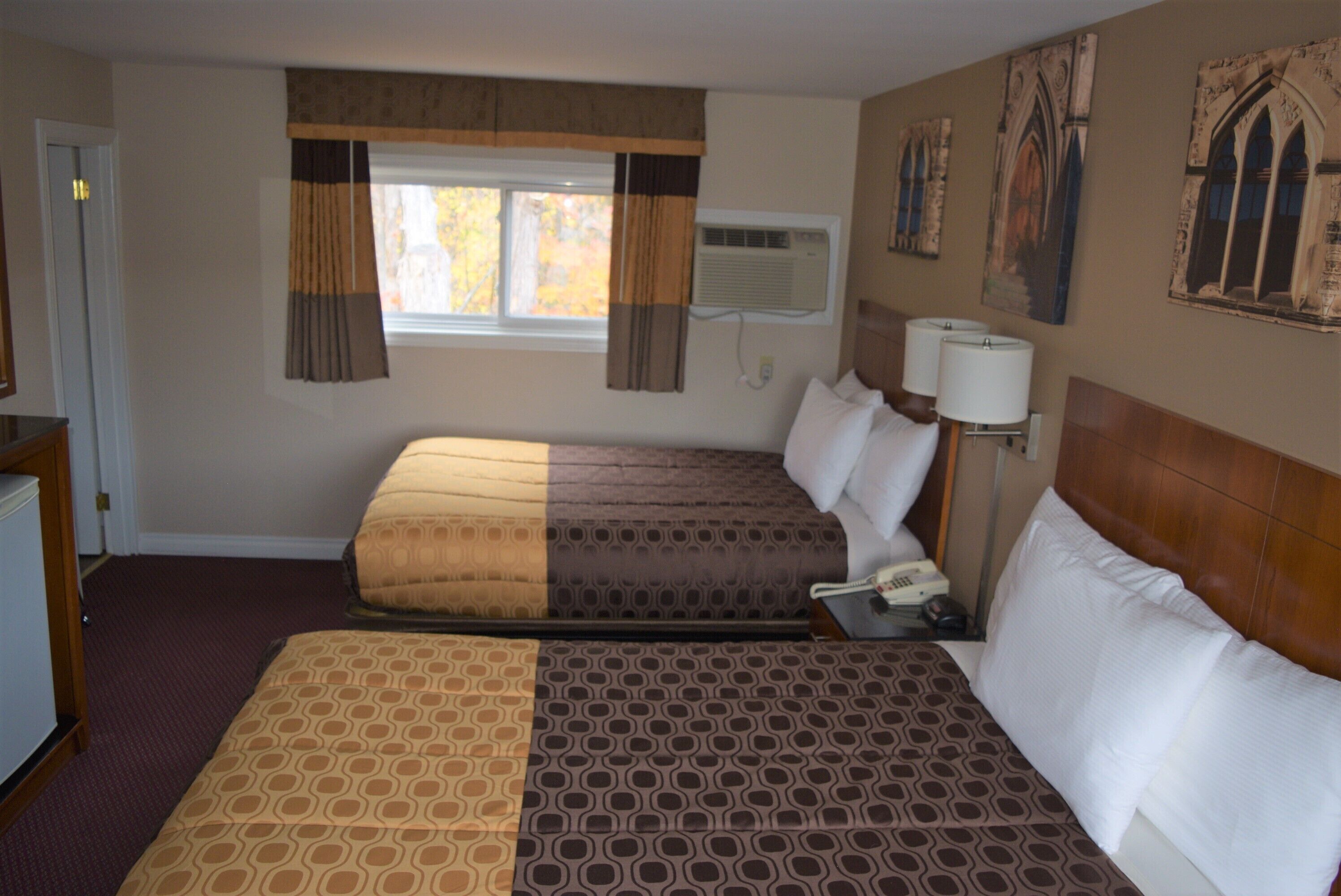 A hotel room with two beds, a desk, a telephone, and a window with curtains.