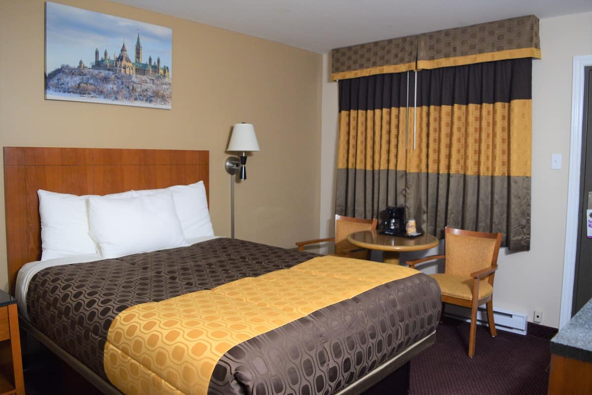 A hotel room with a bed, a chair, a table, and a lamp.