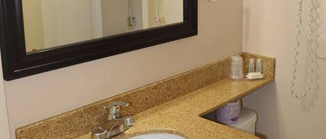 A bathroom with a granite countertop sink, a mirror, a toilet, and a hairdryer on the wall.