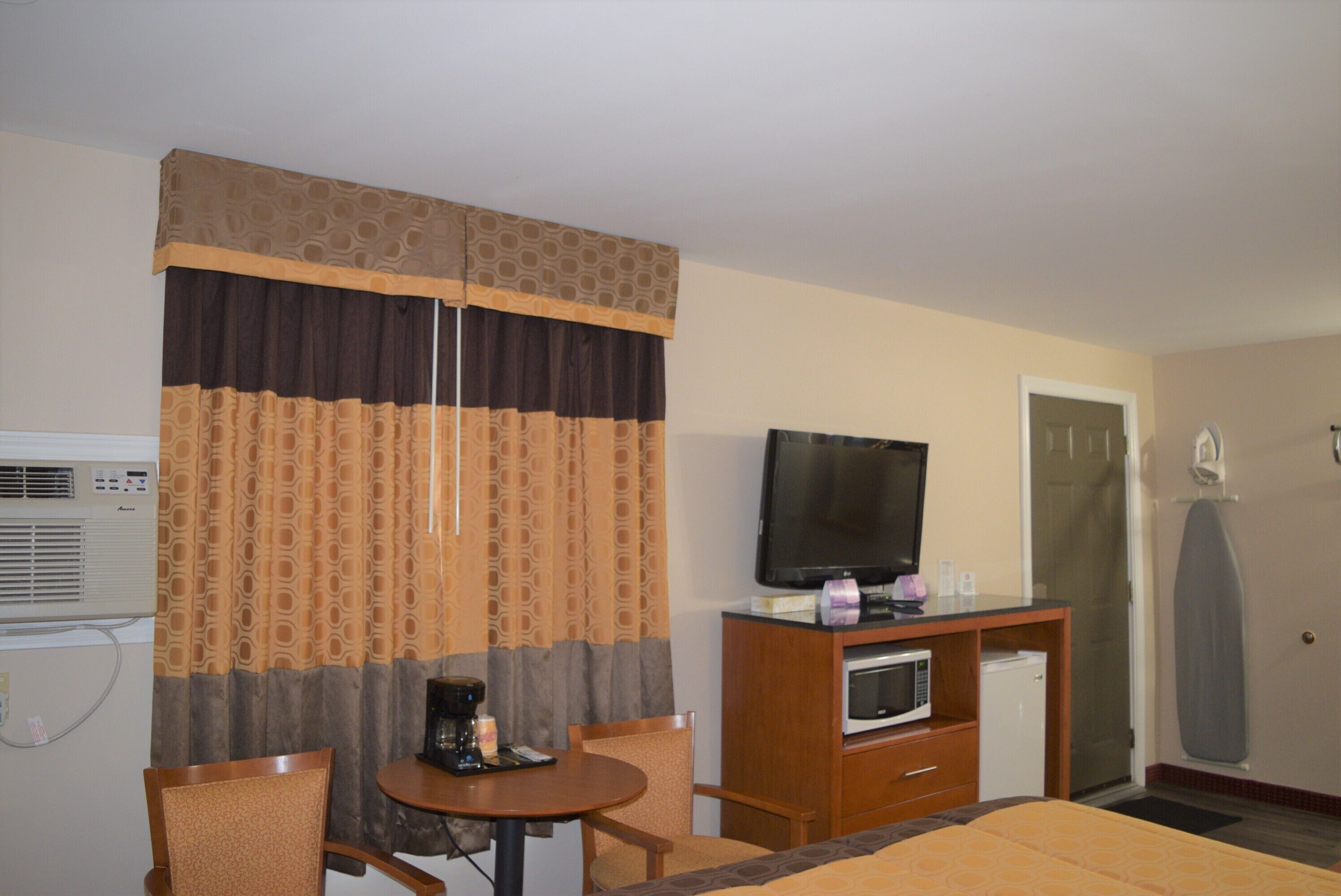 A hotel room with a bed, a TV, a microwave, a coffee maker, and a desk with a chair.