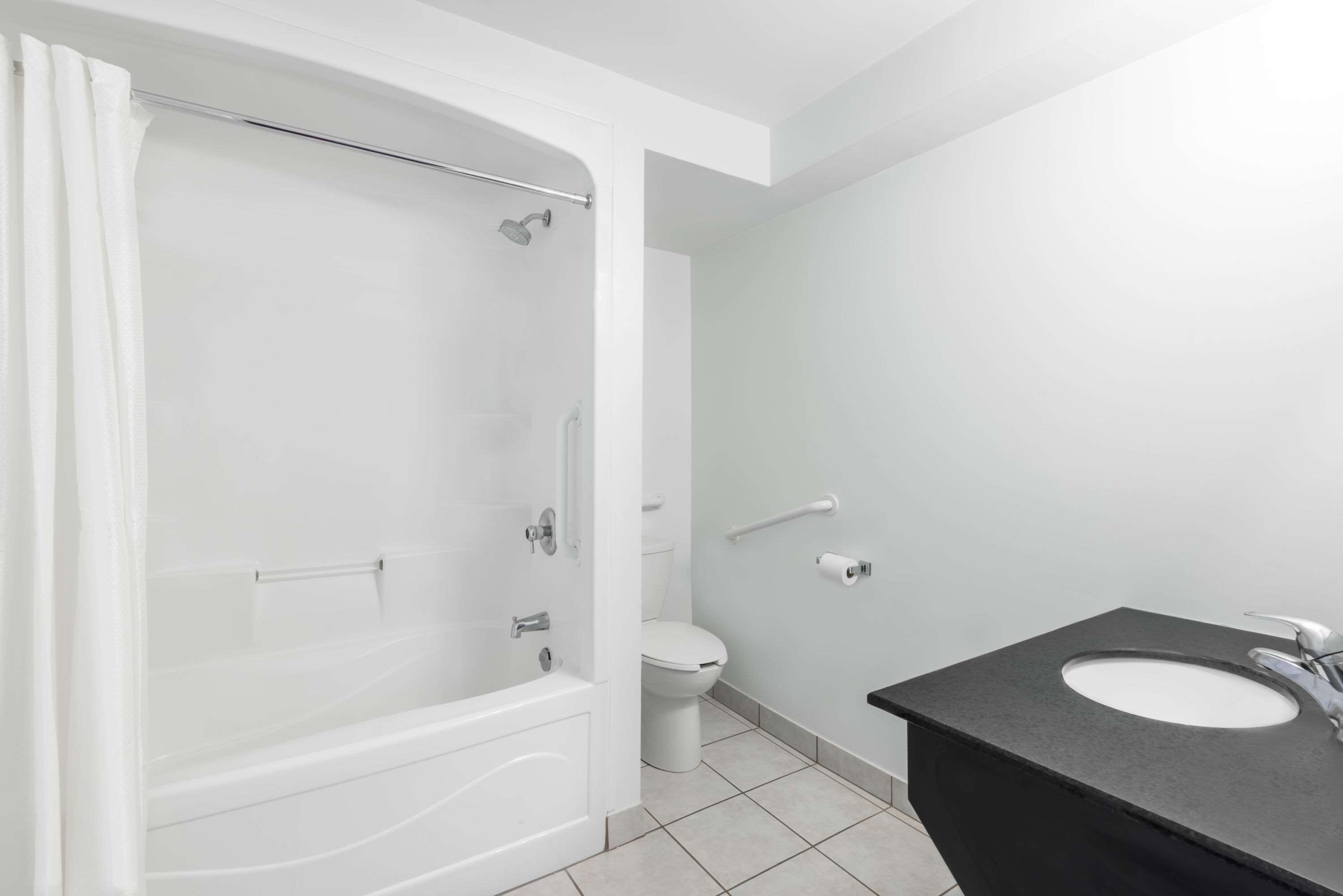 Une salle de bain moderne dotée d’une douche à l’italienne, de toilettes et d’un lavabo avec un plan de toilette noir.