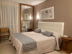 Une chambre d’hôtel avec un grand lit, une chaise, une table de chevet, un miroir et une œuvre d’art accrochée au mur.