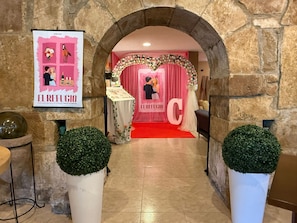 Une arche mène à l'espace réservé à la réception de mariage, où l'on trouve un tapis rouge, des décorations florales et un grand panneau en forme de « C ».