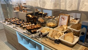 A buffet with various baked goods, including pastries and bread, arranged on a wooden counter with a glass display case. - Hotel El Refugio (Alfoz de Lloredo)