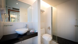 A modern bathroom with a large mirror, a white sink, a black countertop, a white toilet, and a glass-enclosed shower area.